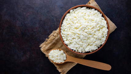 Cottage cheese on a burlap. Fresh cottage cheese and wooden spoon on a dark background. Soft cheese...