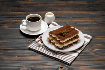 Classic tiramisu dessert on ceramic plate, milk or cream and cup of coffee on wooden background