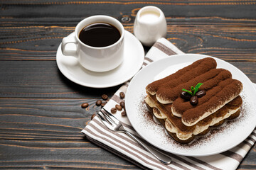Classic tiramisu dessert on ceramic plate, milk or cream and cup of coffee on wooden background