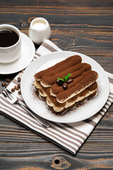 Classic tiramisu dessert on ceramic plate, milk or cream and cup of coffee on wooden background