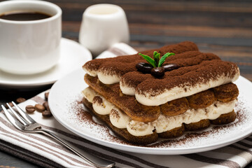 Fototapeta na wymiar Classic tiramisu dessert on ceramic plate, milk or cream and cup of coffee on wooden background