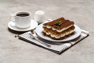 Classic tiramisu dessert on ceramic plate, milk or cream and cup of coffee on concrete background