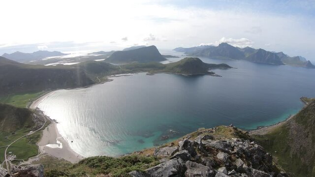 A panoramic panning shot of Uttakleiv beach on the right side and Haukland beach on the left. Small farms and green fields next to white sand beaches in Lofoten, Norway.