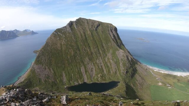 A panoramic panning shot of Uttakleiv beach on the right side and Haukland beach on the left. Small farms and green fields next to white sand beaches in Lofoten, Norway.