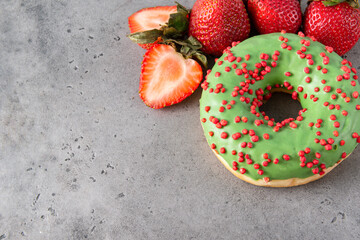 donut with green glaze and red sprinkles, fresh whole,  half strawberries on a gray