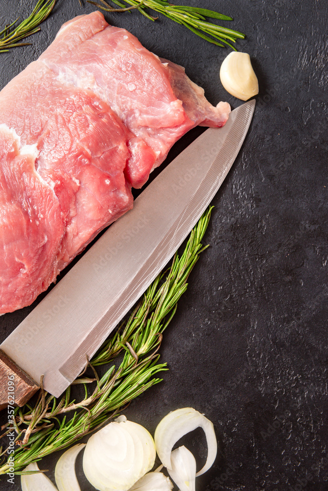 Wall mural piece of raw meat with garlic, rosemary, onion, knife on a black , pork