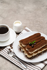 Classic tiramisu dessert on ceramic plate, milk or cream and cup of coffee on concrete background