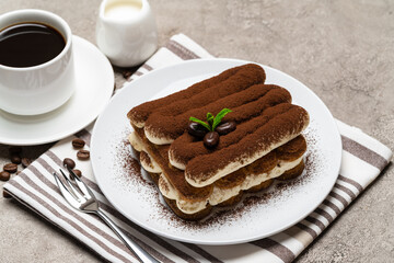 Classic tiramisu dessert on ceramic plate, milk or cream and cup of coffee on concrete background