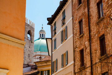 Close up. The view of the azure dome of the central cathedral (duomo) through vintage Italian buildings with shutters, balconies, tiled roofs in the historical centre of Brescia, Lombardy, Italy.