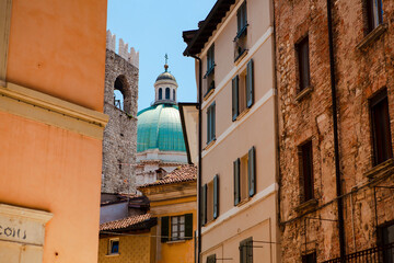Close up. The view of the azure dome of the central cathedral (duomo) through vintage Italian buildings with shutters, balconies, tiled roofs in the historical centre of Brescia, Lombardy, Italy.