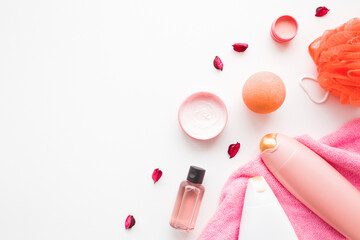 Cream jars, shower bottles, essential oil, pink towel, orange wisp and bath ball or bomb on white table background. Relax products for body washing. Empty place for text or logo. Top down view.