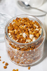 jar of sweet granola with coconut and nuts on white background, vertical