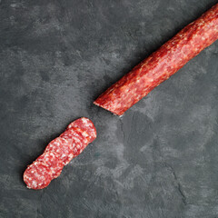 Stick of smoked sausage, salami or boar on a dark graphite background