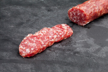 Stick of smoked sausage, salami or boar on a dark graphite background