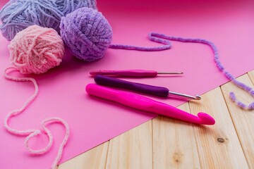 Pink yarn for knitting, knitting needles and hooks. Pink and wood background. Needlework concept. Pink and wood background