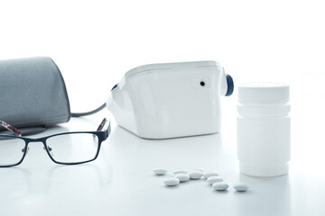 white pills scattered from plastic jar in front of blood pressure monitor, toned, glasses