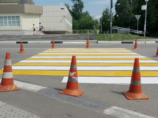 Orange traffic signal cones on the road block a pedestrian crossing that has been painted.