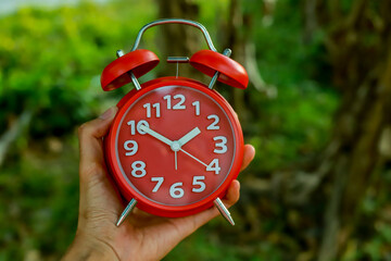 Hand Holding Red Alarm Clock On Bokeh Background