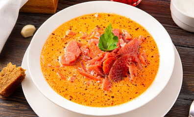 borscht with sour cream and parsley in a white plate on a  wooden background, red  russian  soup close up