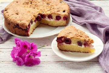 Homemade cherry pie and slice on plate with lilac napkin and flower.