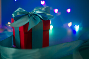 red gift box with a blue ribbon on a blue background with colored lights