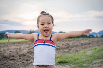 Portrait of Asian child girl smiling and looking at the camera with arms up in summer park at sunset. childhood lifestyle concept.