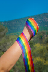 Caucasian hand fist holding rainbow ribbon at the outdoors with clear blue sky. Lgtbiq concept