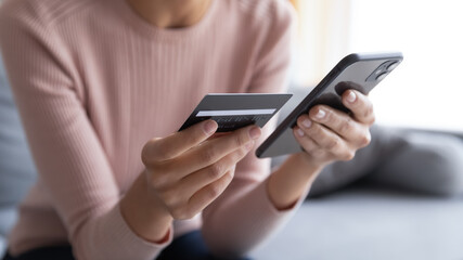 Close up female hands holding credit card and smartphone, young woman paying online, using banking...