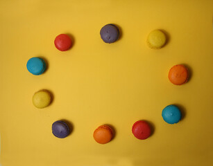 Round frame of macaroons of different colours isolated on yellow background flat lay