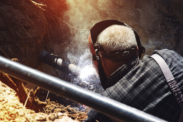 A worker in the pit welds pipes using a welding machine.