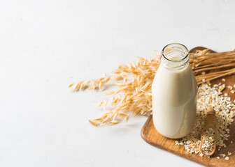 Oat milk in glass bottle with flakes and spike or ears of grain on white background
