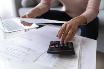 Close up woman using calculator, checking domestic bills, sitting at table with papers at home,...