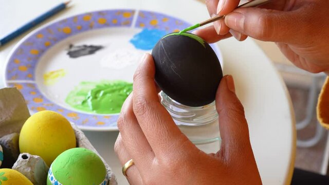 Hands painting details on a black easter egg