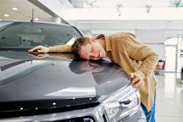 portrait of young caucasian male dreaming about new car in dealership, handsome guy want to buy luxurious auto in dealership. cars, automobile, shopping concept