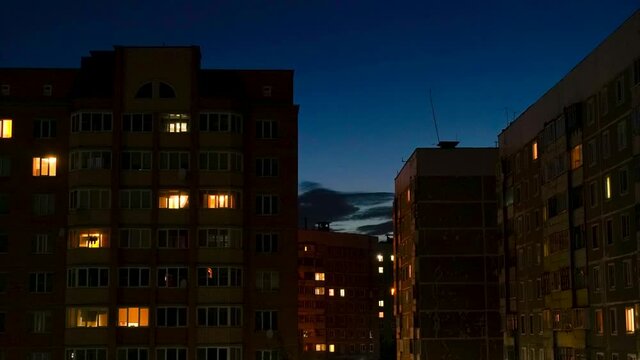 Timelapse of the city, with old houses, an orange sunset, and clouds are floating, lights are lighting up in the windows.