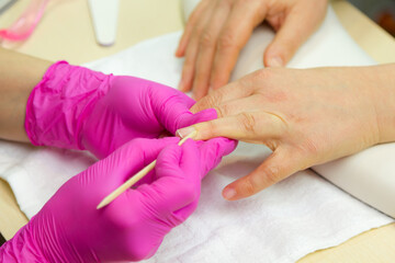 Nail care. Closeup of beautiful woman hands getting manicure in spa salon. Female manicurist cleaning cuticle with professional manicure pusher tool. Cosmetic procedure..