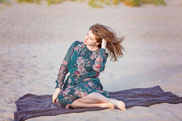 A young girl in a green dress is sitting on the seashore. The wind ruffles her hair