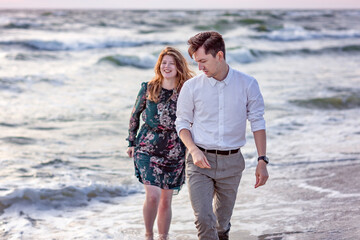 Young happy couple walking on the beach. The sea is behind them. Love, trust, always be together concept