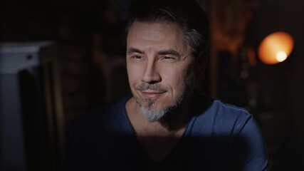 Facial portrait of mature man in his 50s at home sitting in dark living room.