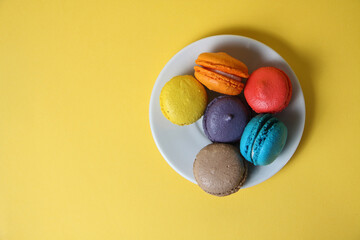 Macaroons of differrent colours on a saucer isolated on yellow background flat lay