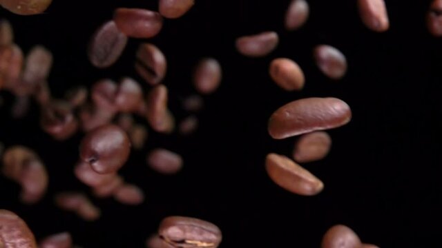 Close-up of roasted coffee beans flying diagonally on the black background in slow motion