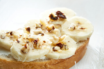 Sandwich with banana slices sprinkled with nuts close up on white wooden table.