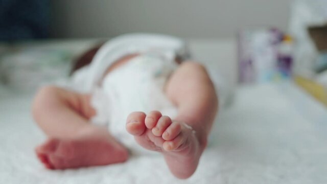 Little legs of a newborn baby. The baby moves a leg. Defocus. New life. Baby in the diaper on swaddling table indoors