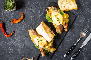 Sandwich with Eggs Benedict, bacon and salad on black stone background