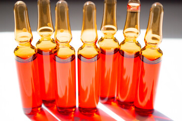 Seven red ampoules standing horizontally close-up on a white background backlit by sunlight. Vitamin B12.