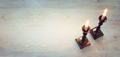 two shabbat candlesticks with burning candles over wooden table. top view