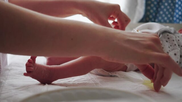 Mother changing diaper on her newborn baby in nursery on swaddling table indoors. Little legs of a newborn baby. The child moves his legs. New life. Dry skin of the baby.