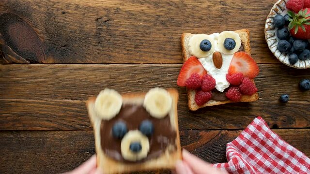 Kids breakfast idea food art funny toasts with chocolate spread, fruits and berries on a wooden table. Children's food concept