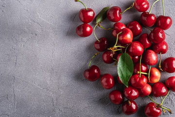 Fresh ripe cherry fruits with green leaves, summer vitamin berries on grey stone background, top view copy space