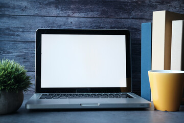 Laptop with blank screen and stack of books on table.